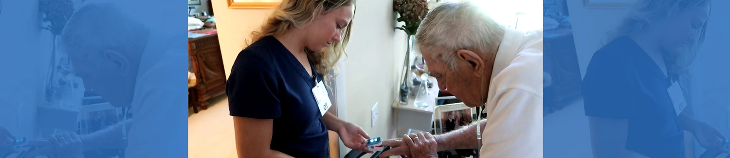 A healthcare worker assists an elderly man by checking his finger with a medical device at home.