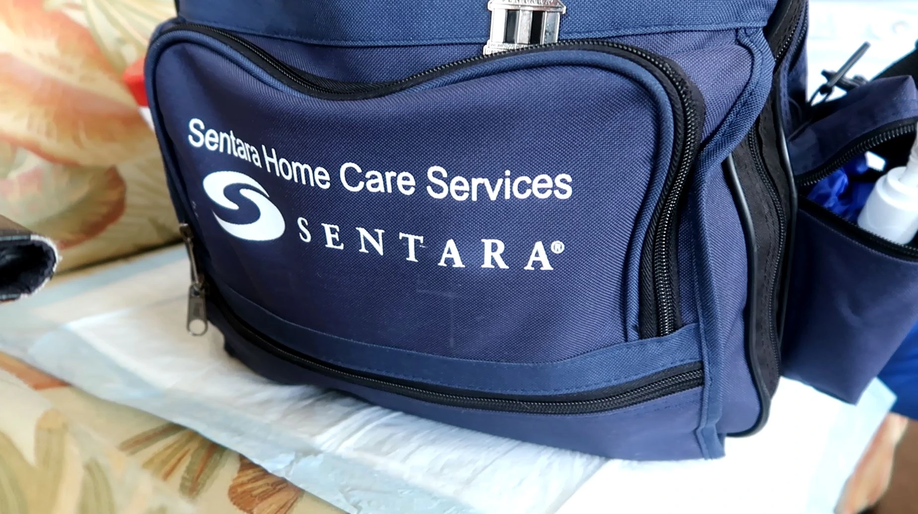A close-up of a blue Sentara Home Care Services bag with the Sentara logo, resting on a surface.