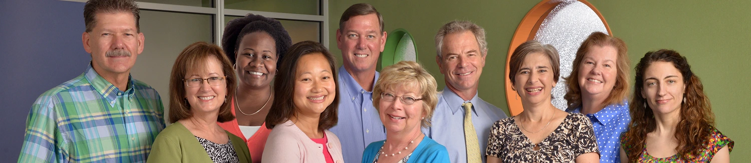 A group of smiling professionals, both men and women, standing together for a group photo indoors.