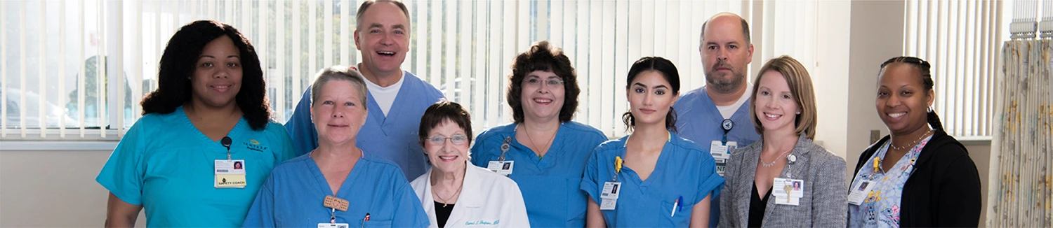 A group of healthcare professionals in scrubs and lab coats, smiling together in a well-lit medical setting.