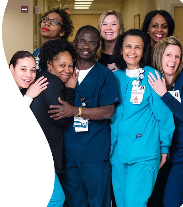 A diverse group of smiling healthcare professionals in scrubs and uniforms gather closely for a group photo.