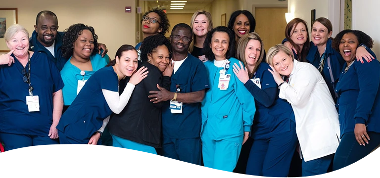 A diverse group of smiling healthcare professionals in scrubs and uniforms gather closely for a group photo.