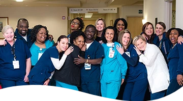 A diverse group of smiling healthcare professionals in scrubs and uniforms gather closely for a group photo.