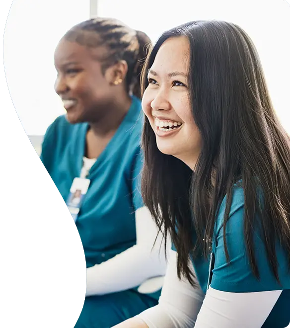 Smiling healthcare workers wearing teal-colored scrubs sit together in a bright room