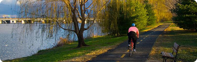 Cyclist rides along a scenic riverside trail lined with trees during golden hour in Northern Virginia.