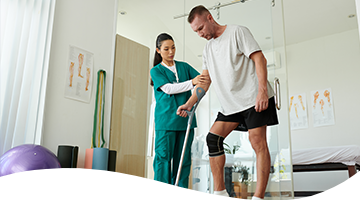 Physical therapist assisting a man with a knee brace during rehabilitation exercises in a clinic.