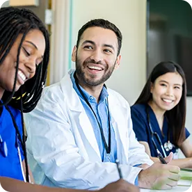 Smiling medical professionals in scrubs and a lab coat sitting at a table.